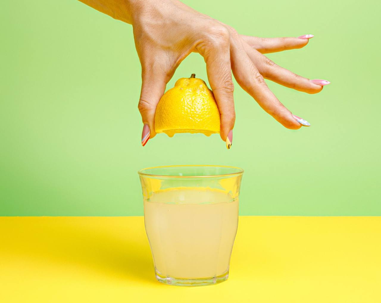 Espremendo meio limão à mão sobre um copo de limonada